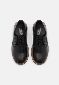 Scarpe in pelle nera con una superficie liscia, punta rotonda e design con lacci. Presentano una suola in pelle marrone con un accento cucito. Marchio visibile.