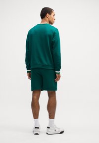 Tyrkysová mikina a odpovídající šortky z měkké tkaniny, s kulatým výstřihem a žebrovanými manžetami. Bílé tenisky doplňují outfit.