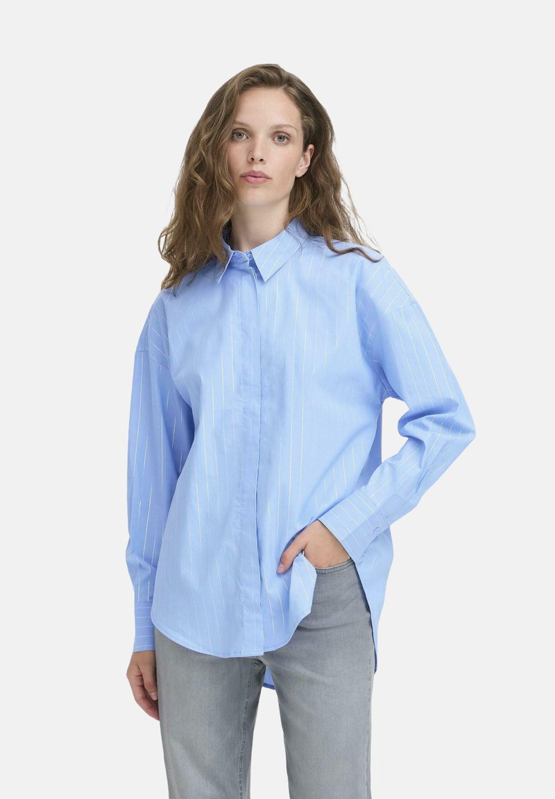 Light blue button-up shirt with white vertical stripes, long sleeves, relaxed fit, and a classic collar. Worn with gray denim pants.