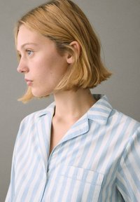 Camisa a rayas azul y blanca con cuello de pico y un bolsillo en el pecho, hecha de una tela ligera, con un corte relajado.