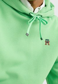 Felpa verde menta realizzata in morbido cotone, dotata di cappuccio con cordoncino, dettagli metallici e un piccolo logo ricamato sul petto.
