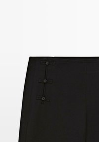 Black fabric skirt with three decorative buttons and bows aligned vertically near the waistband on the left side.