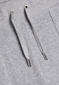 Pantaloni della tuta grigi con una trama morbida, caratterizzati da un cordino con terminali metallici e un design semplice, adatti per un abbigliamento casual.