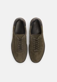 Olive green suede sneakers with round toe, flat laces, and black soles; features subtle stitching details and a smooth leather collar.