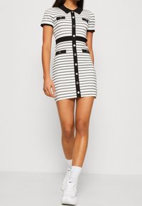 Robe bodycon rayée en noir et blanc, avec un col, des boutons sur le devant et deux poches avant. Fabriquée dans un tissu extensible.