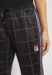 Pantalon noir à carreaux avec des lignes de grille blanches et rouges, bandes latérales bleu marine, blanc et rouge, taille élastique et un petit patch logo "F".