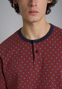 Camicia di tessuto rosso con colletto blu navy e pois blu, dotata di due bottoni al collo. Morbido al tatto e design informale.