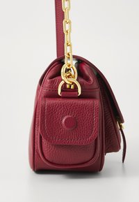 Red leather handbag with a structured shape, a front pocket, gold hardware, and a chunky chain strap. Textured surface with a smooth finish.