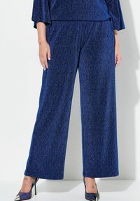 Pantaloni a gamba larga blu in un tessuto strutturato con riflessi metallici, abbinati a tacchi a punta con un accento argentato a contrasto.