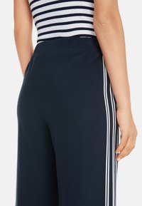 Marineblaue weite Hose aus weichem Stoff, mit weißen Seitenstreifen und einem bequemen Bund. Die Rückansicht hebt die Passform hervor.