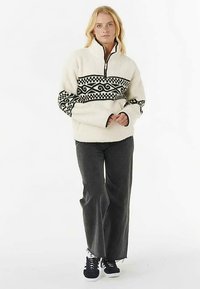 Fleece pullover in cream with a black geometric pattern across the chest, featuring a half-zip design and relaxed fit. Textured sleeves.