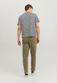 Gestreiftes T-Shirt in Marineblau und Weiß, kurze Ärmel. Olivgrüne Hose mit slim fit. Weiße Sneaker mit schwarzen Akzenten.