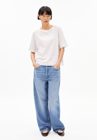 Striped t-shirt in white, red, and blue, with a relaxed fit and short sleeves. Paired with wide-leg blue denim jeans. Black flat shoes.
