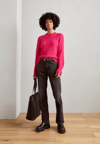 Fuchsia gebreide trui, zwarte high-waisted jeans, chunky zwarte platform schoenen en een zwarte tote bag. Gestructureerde stof en minimalistisch ontwerp.