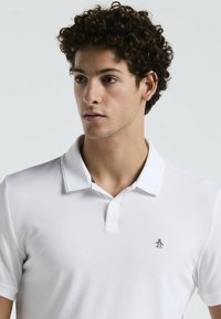 Witte poloshirt van textuurstof, met een klassieke kraag en drie knopen, voorzien van een klein pinguïnlogo op de borst.