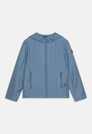 Veste capuche bleu clair avec un design matelassé, deux poches zippées et un emblème de marque sur la manche gauche. Matériau lisse et léger.
