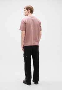 Světle fialové bavlněné tričko s krátkým rukávem, spárováno s černými cargo kalhotami s bočními kapsami a rovnými nohavicemi.