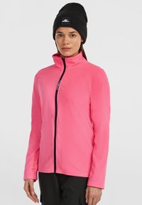 Fleece jaka spilgtā rozā krāsā, ar augstu apkakli, pilnu rāvējslēdzēju un melnām akcentiem, ar teksturētu virsmu un Polartec zīmolu uz piedurknes.