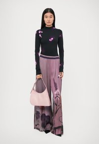 Black long-sleeve top with purple floral print, paired with purple wide-leg pants featuring a floral pattern, holding a light pink handbag.