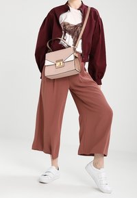 Bordový bomber svetr přes bílý grafický tričko, hnědé široké kalhoty a bílé tenisky. Béžová kabelka s geometrickými akcenty.