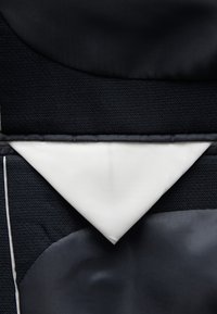 Textile noir et bleu marine foncé avec des textures variées ; inclut un accent triangulaire blanc. Présente des coutures et des formes géométriques.