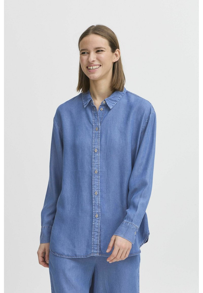 Camicia in denim blu con chiusura frontale a bottoni, maniche lunghe e colletto classico. Texture morbida con una vestibilità rilassata e dettagli cuciti.