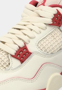 Άσπρο δερμάτινο αθλητικό παπούτσι με κόκκινες λεπτομέρειες, τμήματα από δίχτυ, υφασμένα κορδόνια και καμπυλωτό σχήμα. Φέρει ξεχωριστό λογότυπο πάνω από τα κορδόνια.