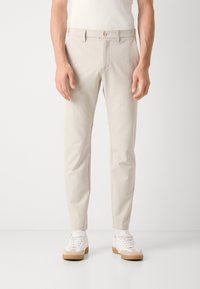 Chinos bege com corte reto, apresentando um fecho de botão único, bolsos laterais inclinados e uma textura suave. Combinados com ténis brancos.