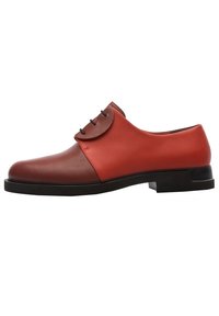 Chaussure en cuir avec sections contrastantes rouges et marron, bout arrondi, semelle plate et cinq œillets pour les lacets. Design élégant et moderne.