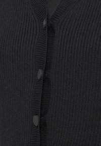 Κοντινό πλάνο από μαύρο πλεκτό κασκόλ με τρία ματ μαύρα κουμπιά κλεισμένα κατά μήκος του κέντρου μπροστά.