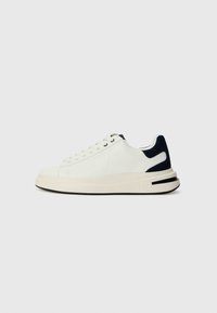 Hvite lave sneakers med marineblå detaljer, teksturert overflate, flate lisser, tykk såle og preget logo på siden.