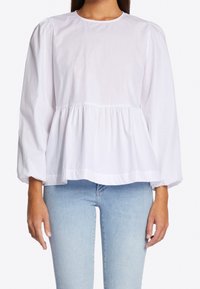 Donna che indossa una blusa peplum bianca a maniche lunghe con maniche a sbuffo abbinata a jeans azzurri, vista dalle spalle ai fianchi.