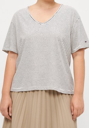 Persoon die een wit T-shirt met korte mouwen en een V-hals draagt met dunne zwarte horizontale strepen en een beige geplooide rok, zichtbaar van nek tot heupen.