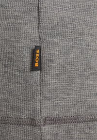 Gros plan sur un tissu gris à maille gaufrée avec une petite étiquette noire montrant le mot "BOSS" en lettres orange.