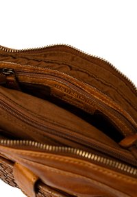 Interno di una borsa in pelle marrone con più scomparti con zip e un'etichetta logo cucita visibile che legge "RE-DESIGNED Est. 2005".