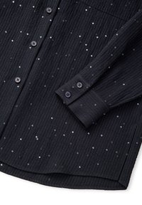 Czarna koszula zapinana na guziki z teksturowanej tkaniny w pionowe paski i rozmieszczonymi srebrnymi cekinami. Szczegółowe mankiety z dwoma guzikami.