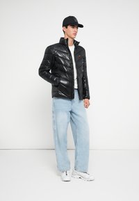 Juodas pūkinis švarkas su blizgia apdaila, puoštas įstrižomis siūtomis dalimis ir aukšta apykakle. Derinamas su šviesiai mėlynomis plačiomis džinsų kelnėmis ir baltais sportbačiais.