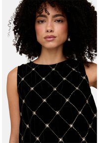 Schwarzes ärmelloses Samtkleid mit einem Diamantmuster, das in Gold umrandet ist, mit Blumenverzierungen an den Schnittpunkten.