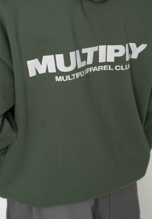 Zelená mikina s nápisom "MULTIPLY APPAREL CLUB" v bielom tučnom písme. Má voľný, skrátený strih a mäkkú bavlnenú tkaninu.