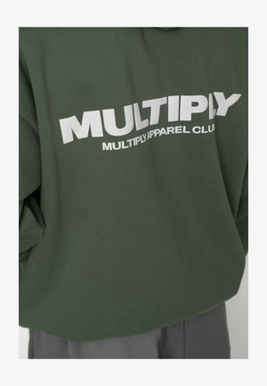 Hanorac verde cu textul "MULTIPLY APPAREL CLUB" imprimat cu litere albe îndrăznețe. Prezintă un design larg, cropped și o țesătură moale din bumbac.