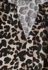 Leopardmönstrad tyg med en blandning av svart, tan och grå färger; har en V-ringning och rynkor längs kragen.