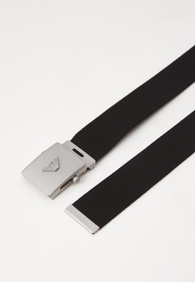 Curea țesută neagră cu o cataramă metalică lucioasă de culoare argintie, având un design cu logo. Catarama include un mecanism de eliberare laterală și accente cu vârf plat.
