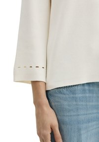 Witte textuur top met driekwartmouwen, voorzien van een gespleten manchetdesign. Gecombineerd met lichtblauwe denim, met een relaxte pasvorm.