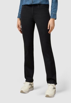 Vaqueros negros de pierna recta con bolsillos frontales, cremallera y pasadores para el cinturón, combinados con zapatillas crema con acentos metálicos.