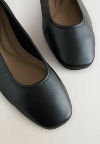 Bailarinas negras de cuero suave, con puntera redonda y plantilla acolchada. Costuras mínimas y diseño elegante.