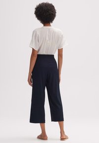 Bílá, texturovaná košile s krátkým rukávem spárovaná s tmavě námořnickými širokými culotty. Oblečení má volný střih a elastický pas.