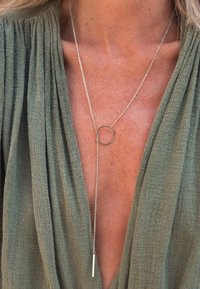 Collier lasso en argent avec fermoir circulaire et pendentif en barre porté sur un haut vert olive texturé à décolleté en V profond.