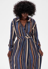 Pasiasta sukienka z kołnierzykiem, z niebieskimi, brązowymi i beżowymi pionowymi paskami, projektem typu kopertowego oraz detalem w postaci guzika w talii.