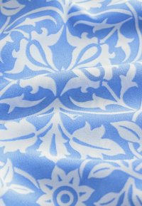 Tessuto blu caratterizzato da un motivo damascato floreale bianco, con una consistenza liscia e una caduta morbida. Il design include foglie e motivi ondulati.