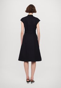 Crna haljina do koljena s kratkim rukavima, suženi struk i lepršava suknja. Glatka tekstura s suptilnim sjajem i detalj s remenom na struku.